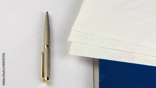 An elegant pen, a book, three envelopes and a small pile of white paper sheets on a wooden desk