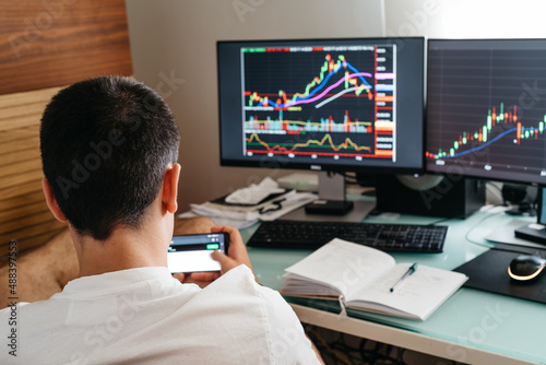 Successful young trader in casual wear working with charts and market reports at home