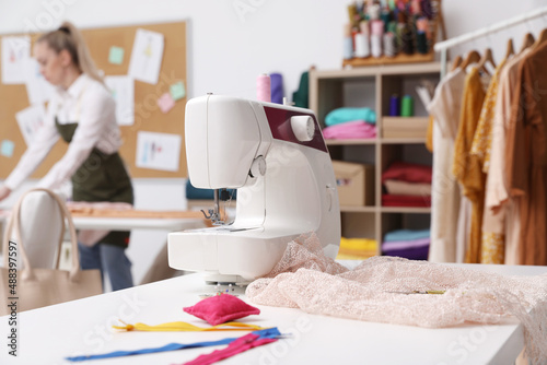 Dressmaker working in atelier, focus on table with sewing machine and accessories