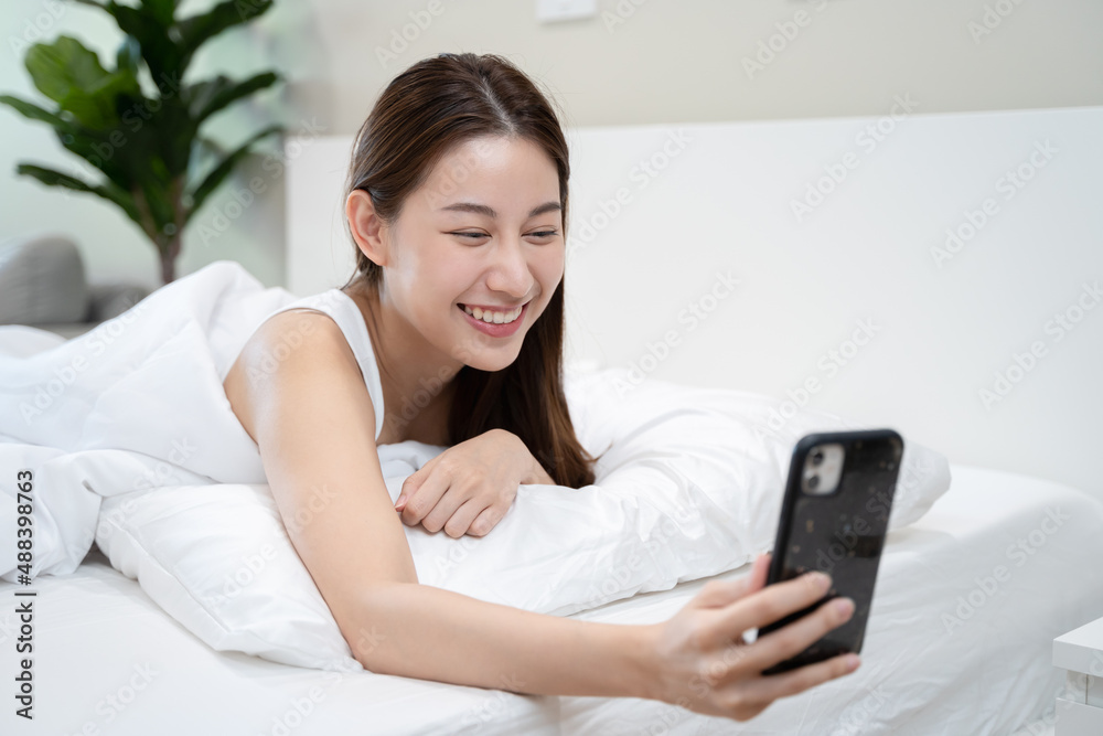 Happy Asian woman conference call via smartphone with her friends on the bed at home Happy Asian woman conference call via smartphone with her friends on the bed at home