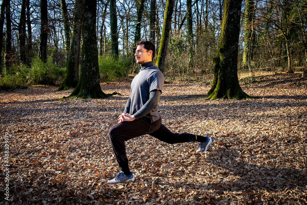 Runner is doing stretching in the woods. Young man with blue eyes and mustache is training in the park. Runner is doing stretching in the woods. Young man with blue eyes and mustache is training in the park.