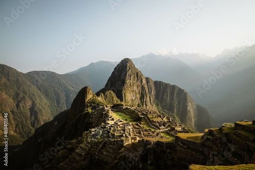 World-famous Inca city of Machu Picchu during sunrise with yellow light rays and misty clouds (without any visitors) (Aguas Calientes, Peru, South America)