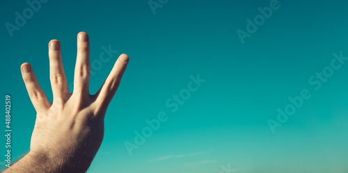 Male hand showing or doing number four gesture on blue summer sky background. Man gesturing number 4 in sign language. Counting down, four fingers up concept idea. Rabia sign. Copy space for text. photo