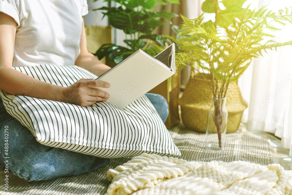 Woman chilling and reading in living room, Artificial plant, Fiddle leaf fig tree, Indoor tropical natural houseplant for home interior and air purification.