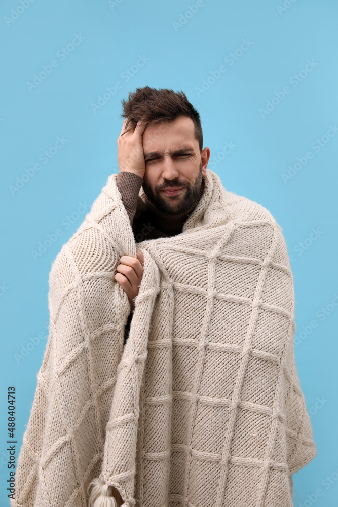 Man wrapped in blanket suffering from headache on light blue background. Cold symptoms Man wrapped in blanket suffering from headache on light blue background. Cold symptoms