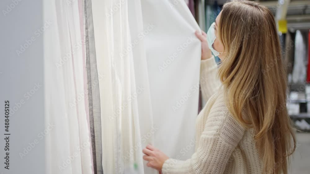young woman in a protective mask close-up in the store chooses home textiles, chooses curtains young woman in a protective mask close-up in the store chooses home textiles, chooses curtains
