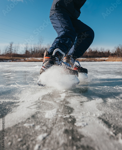 Cropped close up of hockey skates stopping on ice outdoors.