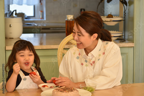 お母さんと一緒にケーキを作りながらいちごを食べる女の子