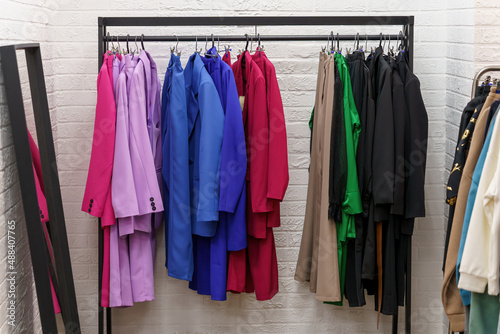Hanger with colorful women's clothes in store near white wall.