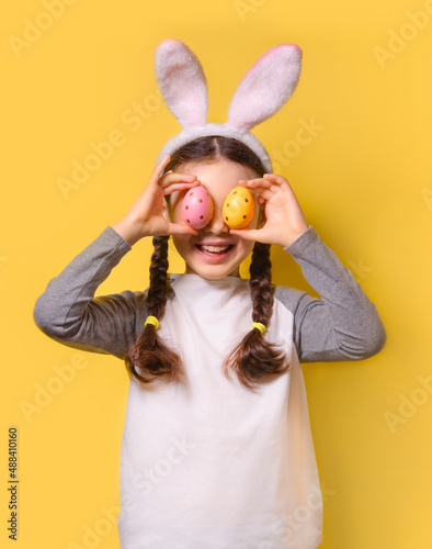 Photography Funny happy girl with Easter bunny ears and colorful Easter eggs on a yellow background