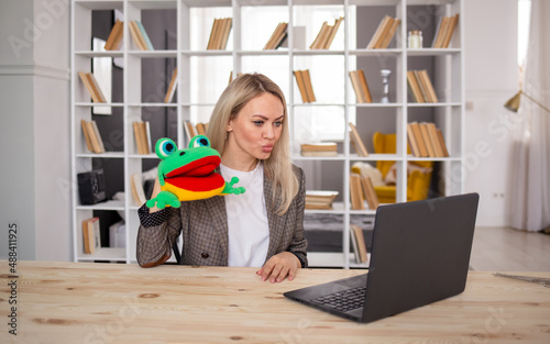 The speech therapist teacher conducts an online lesson remotely with laptop. A female speech therapist shows an exercise with a knitted frog toy