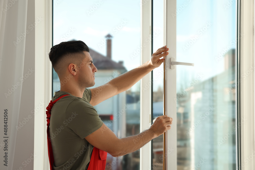 Worker putting rubber draught strip onto window indoors