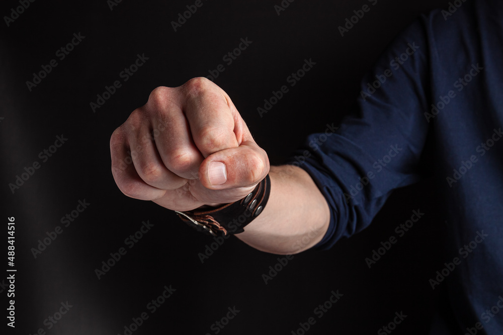 Fototapeta premium Man's hand with a clenched fist on a dark background. Fist threat for fighting, aggressive and angry stance. Domestic violence concept.