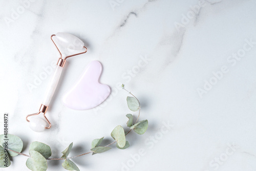 Fototapeta Naklejka Na Ścianę i Meble -  Gua Sha massager and rose quartz massage roller on marble background. Pink jade stone for face and body care. Horizontal shoot. Flat lay, top view. Copy space for your text.