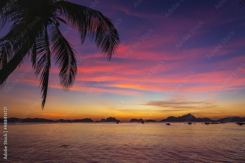 Picturesque tropical sunset. Dramatic evening sky above island. Palm tree and isles silhouettes. Exotic seascape in evening twilight. El Nido lagoon in night dusk. Tropical vacations.