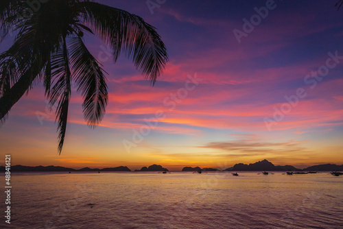 Picturesque tropical sunset. Dramatic evening sky above island. Palm tree and isles silhouettes. Exotic seascape in evening twilight. El Nido lagoon in night dusk. Tropical vacations.