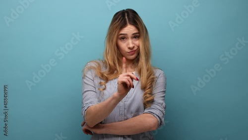Bossy caution. Portrait of serious angry woman pointing finger, showing warning gesture at camera, alarming to be careful, wearing striped shirt. Indoor studio shot isolated on blue background.