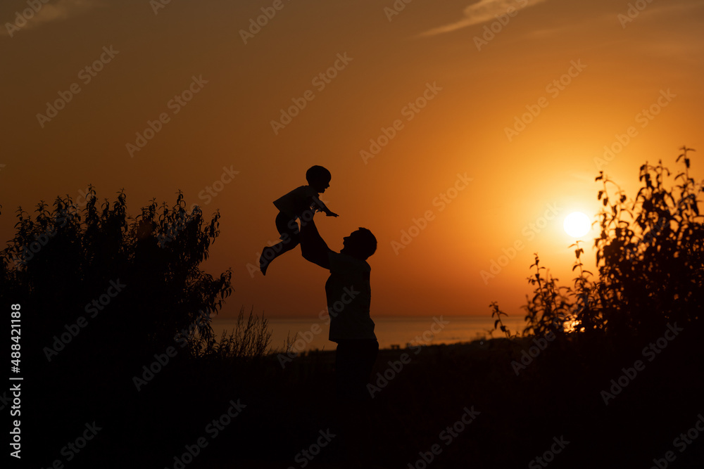Silhouette of a man and a child against the sunset.Dad raises his son 