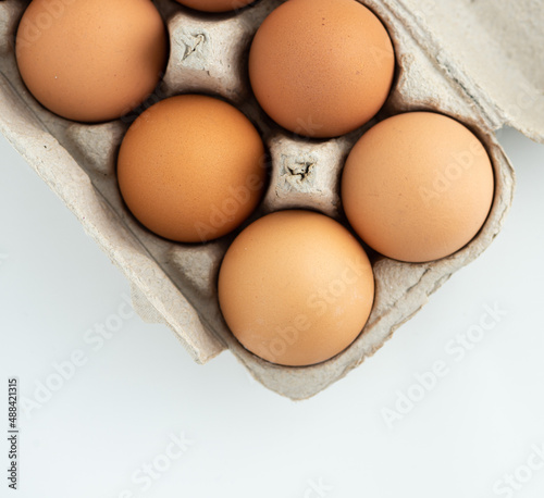 Overhead view of several brown organic eggs in a cardboard carton on a white marble table.