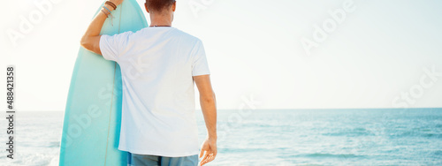 Photography Portrait of surfer in white t-shirt with surf board near the ocean, looking far
