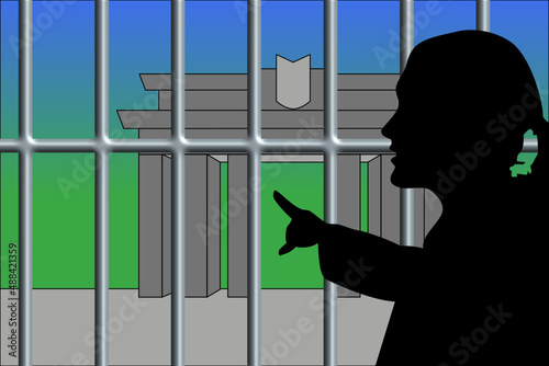 Silhouette einer Frau zeigt durch ein dickes Gitter auf ein Gebäude auf der anderen Seite