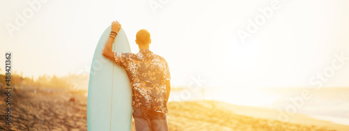 Photography Portrait of happy surfer in hawaiian t-shirt with surf board on the beach, looki