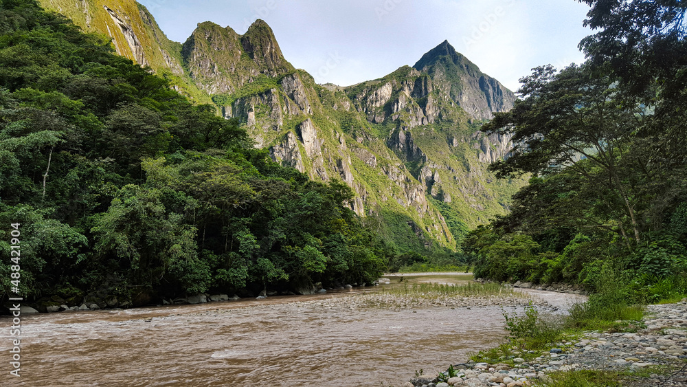 River that crosses through the green mountains, surrounded by bushes and trees. where the sun hides behind the vegetation and shows the great mountains and it's highlights.