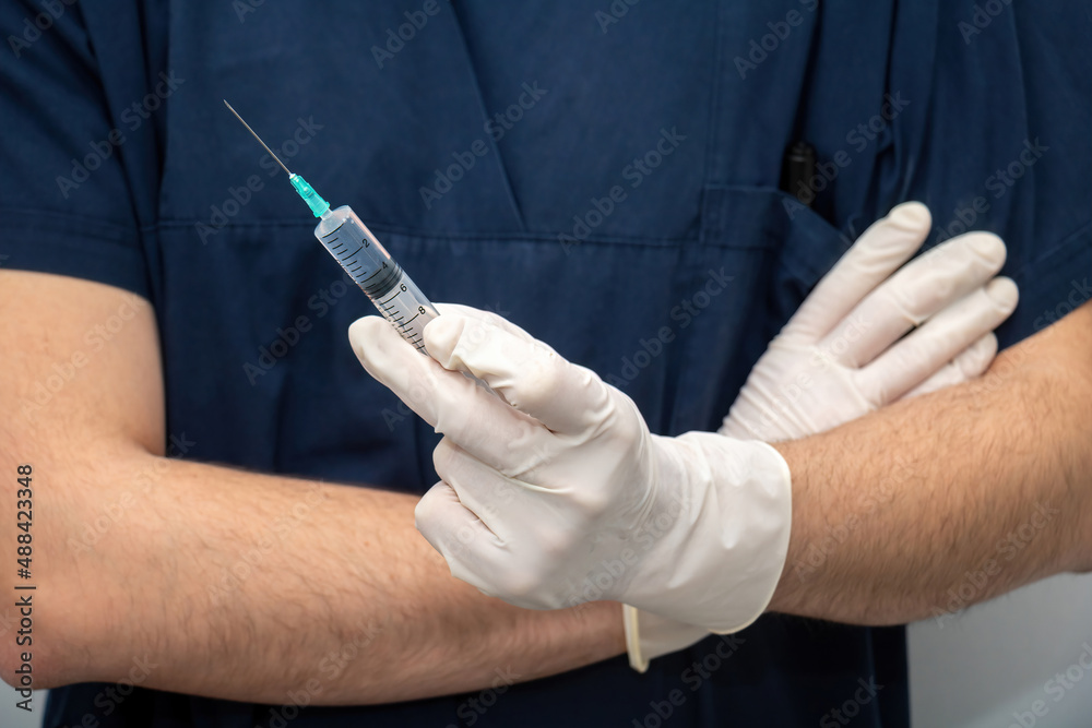 Doctor in medical uniform holds in hand with disposable glove, liquid drug in syringe with needle. Doctor in medical uniform holds in hand with disposable glove, liquid drug in syringe with needle.