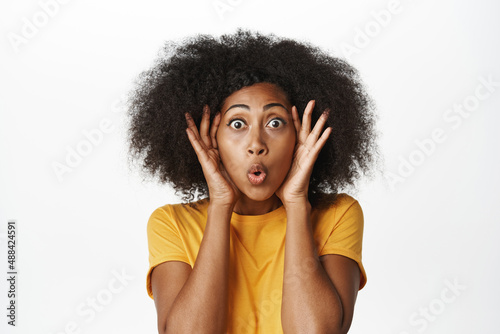 Close up portrait of enthusiastic Black woman gasping, staring amazed at camera, looking with yearning and surprise, standing over white background