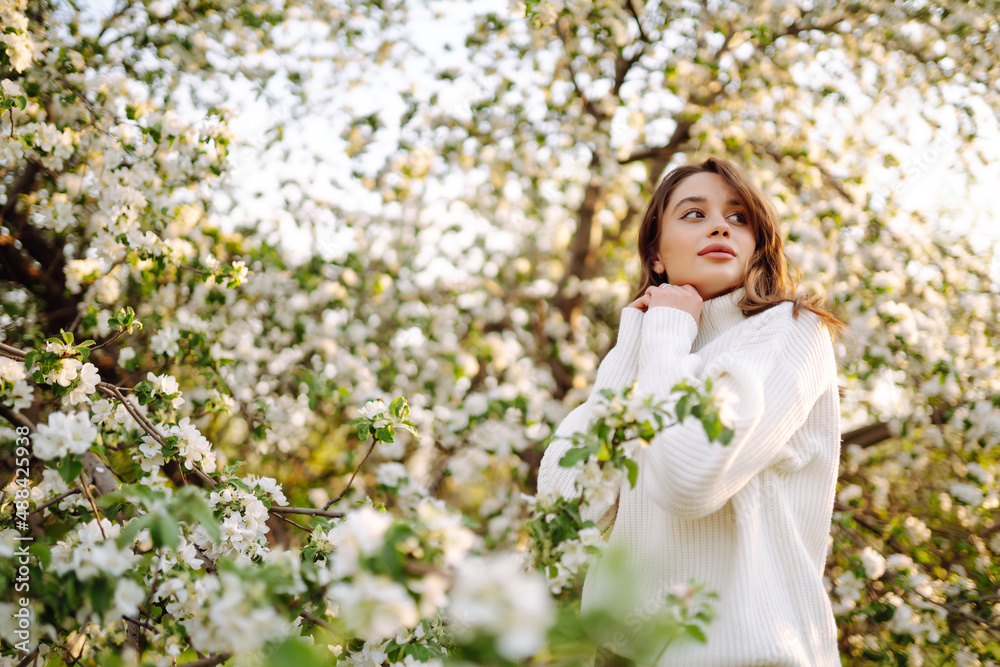 Young woman enjoying scent in blooming spring garden. The concept of relax, travel, freedom and spring vacation. Fashion style