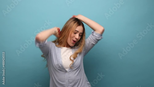 Free positive woman dancing at a disco night club, moving to the rhythm enjoying a festive atmosphere, relaxing, wearing striped shirt. Indoor studio shot isolated on blue background.