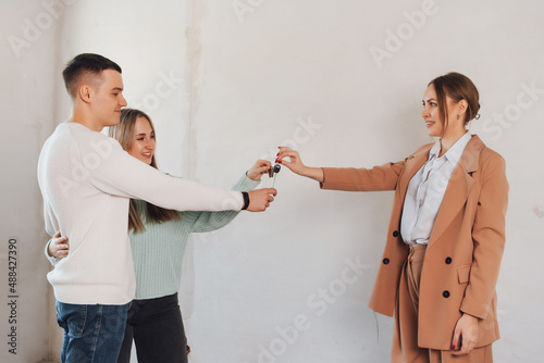 Happy real state agent giving new house key to a young couple.