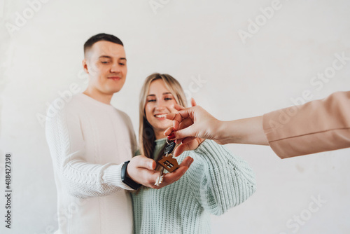 Happy real state agent giving new house key to a young couple. Couple taking keys with house keychain. Couple receiving house key from real estate agent.