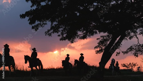Silhouette group of cowboy and girl and American Indian man ride horse on road with background of sunset and evening light.