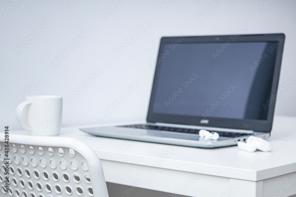 Laptop, white cup, wireless headphones on a white table. Workplace.