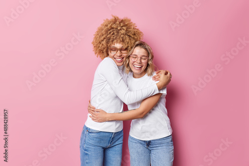 Friendly cheerful optimistic women embrace each other with love and smile gladfully have good relationship feel glad isolated over pink background. Friends spend family day together. Bonding concept photo