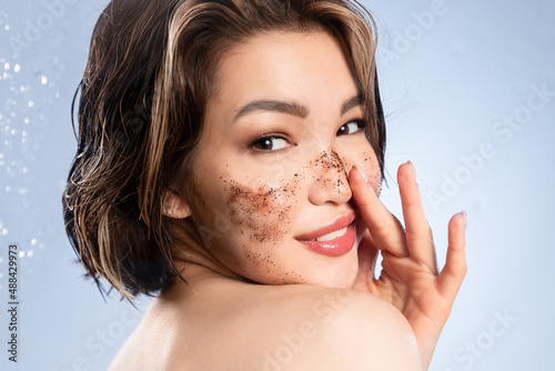 Quadro em tela Playful young asian woman with bare shoulder scrubbing facial skin, cleansing face by cosmetic scrub, removing makeup for glowing pure healthy skin