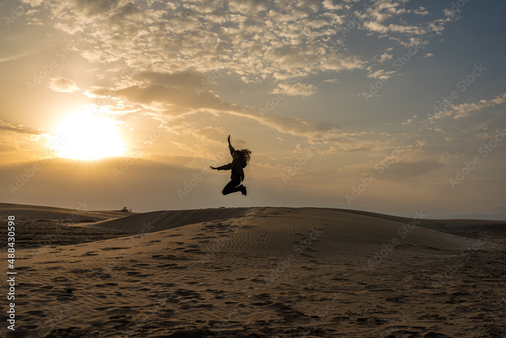 Woman throwing sand on the dunes of a beach at sunset. Freedom