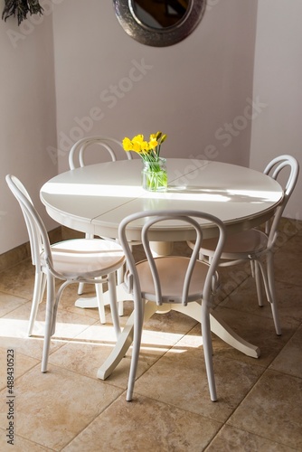 Daffodils in a glass on the table, with chairs in the room