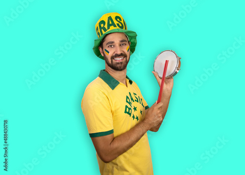 Man smiling with shirt and hat writings of Brazil playing a tambourine. Isolated. Green background photo