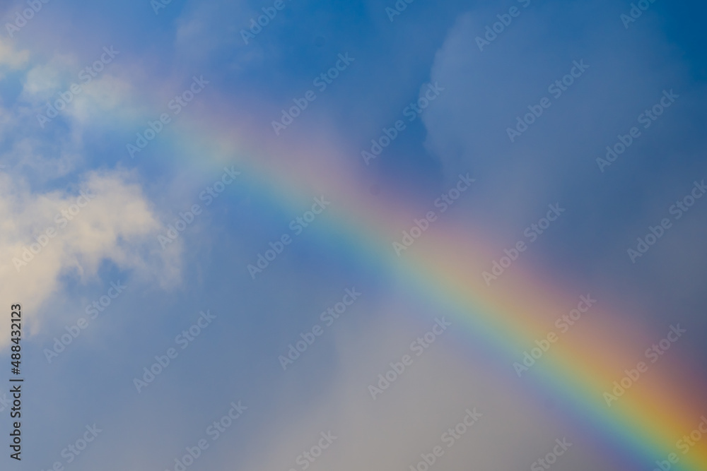 Multicolored rainbow after rain among blue sky clouds