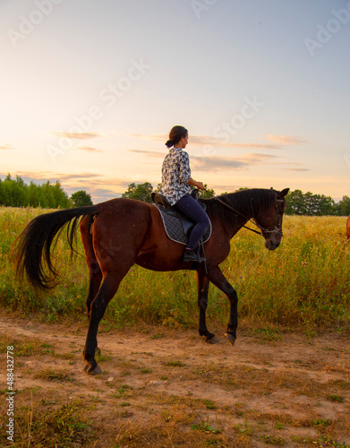  A girl rides a horse in a field on a warm evening at sunset. © FO_DE