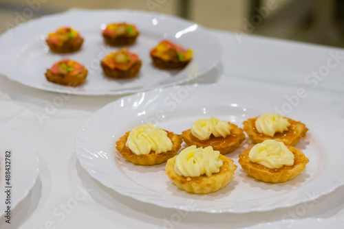 Assortment of delicious fresh shortcrust tart cakes with cream on white plate for sale at restaurant, cafe, bakery. Dessert, culinary, sweet food and confectionery concept