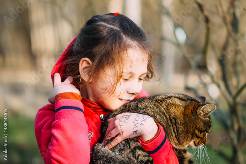 A little hugs her cat outdoors. 