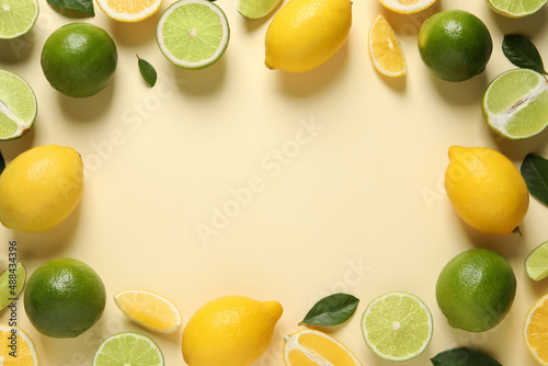 Frame of fresh ripe lemons, limes and green leaves on beige background, flat lay. Space for text