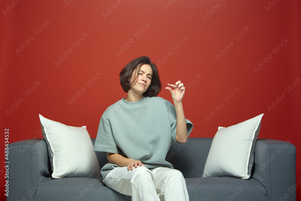 Modern young girl upset about small size of salary, sitting on sofa. Very little money or discounts in online store
