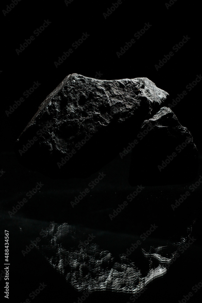 Black textured stones on a dark background lie on a glass surface and, being reflected in it, form unusual figures. A wallpaper for a desktop of a computer or home screen on a mobile phone.