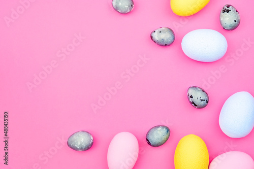 Chicken and quail painted colorful eggs on a pink background with copy space