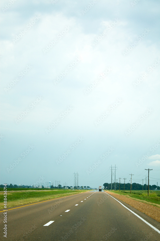Power lines running alongside a wide, flat two-lane highway under a grey cloudy sky.  Image has concept of road trips and has copy space
