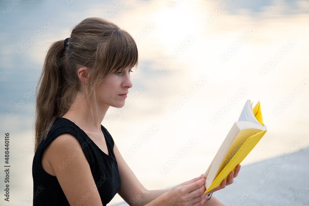 Female student sitting in summer park reading textbook outdoors. Education and sudy concept Female student sitting in summer park reading textbook outdoors. Education and sudy concept